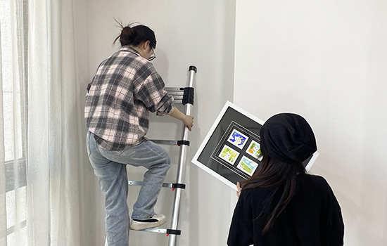 Two girls are using a en131 telescopic ladder to hang a painting