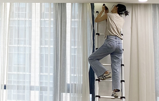 A girl is climbing up a en131 telescopic ladder to repair curtains
