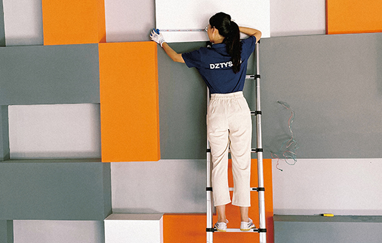 a girl standing on a telescopic aluminum ladder is measuring brick length with a band tape