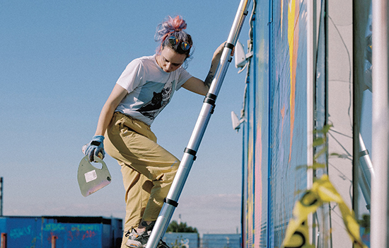 a girl is painting murals with a telescopic extension ladder