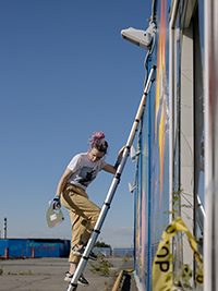 a girl is climbing a telescopic ladder to painting the wall